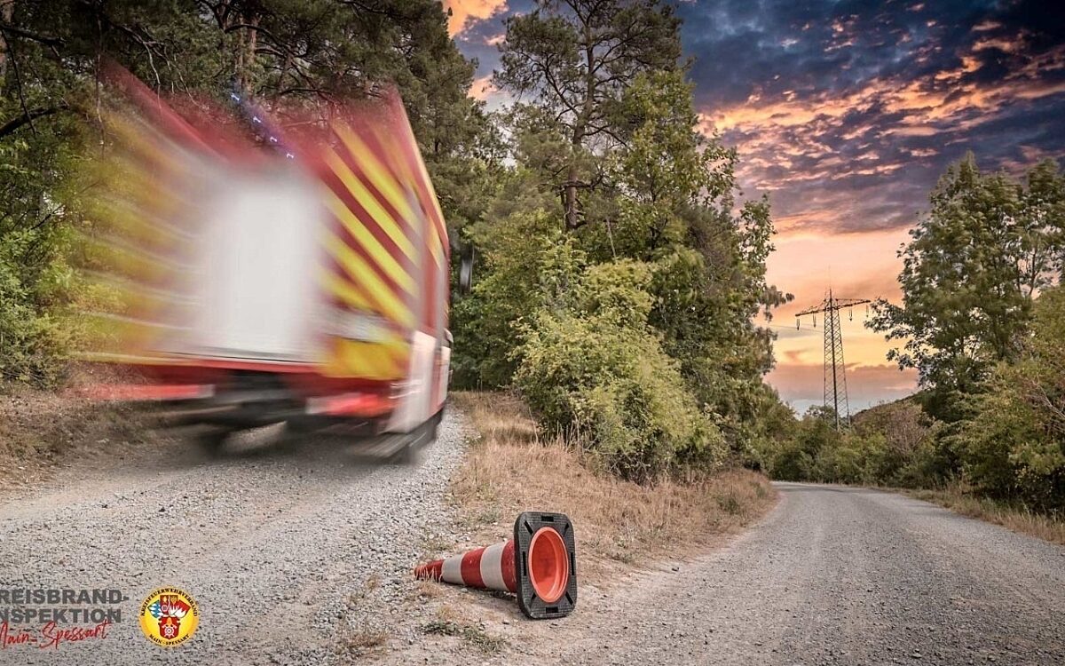Ein Leitkegel der Feuerwehr liegt an einer Weggabelung, ein Feuerwehrfahrzeug fährt vorbei Ein Leitkegel der Feuerwehr liegt an einer Weggabelung, ein Feuerwehrfahrzeug fährt vorbei