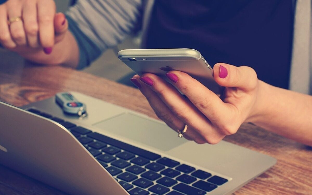 Eine Frau sitzt mit Smartphone am Laptop Eine Frau sitzt mit Smartphone am Laptop