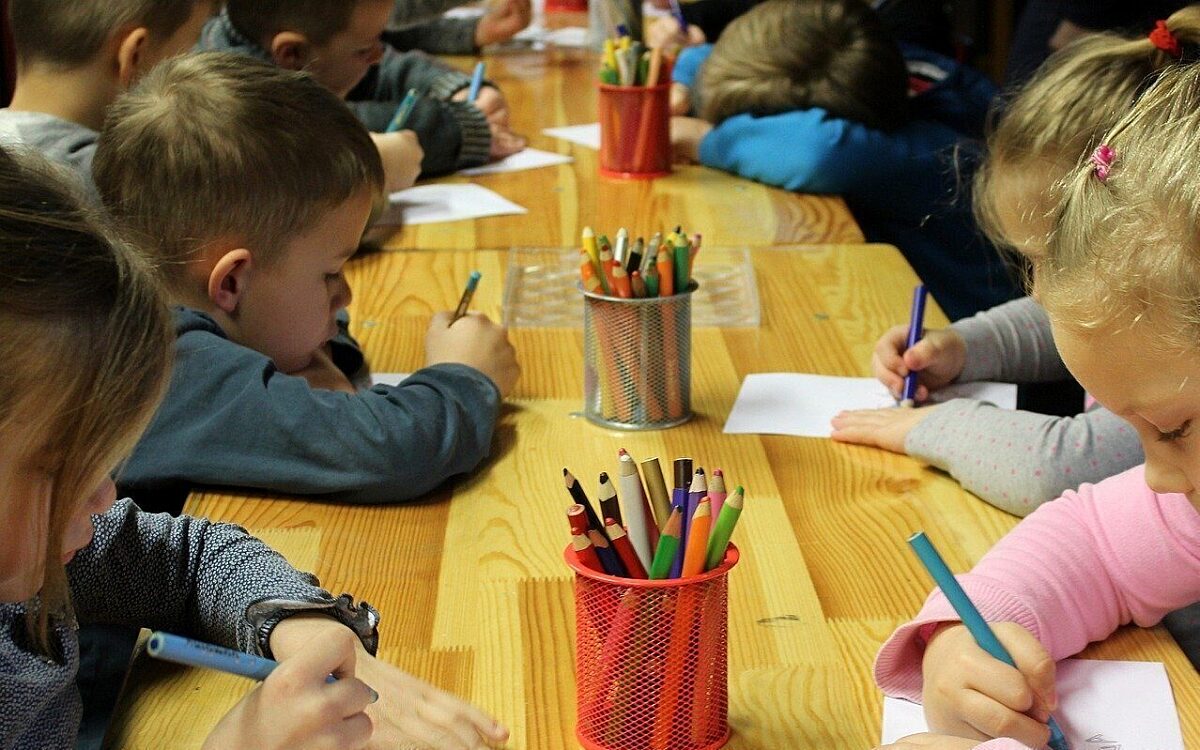 Kindergartenkinder mal an einem großen Holztisch mit Buntstiften Kindergartenkinder mal an einem großen Holztisch mit Buntstiften