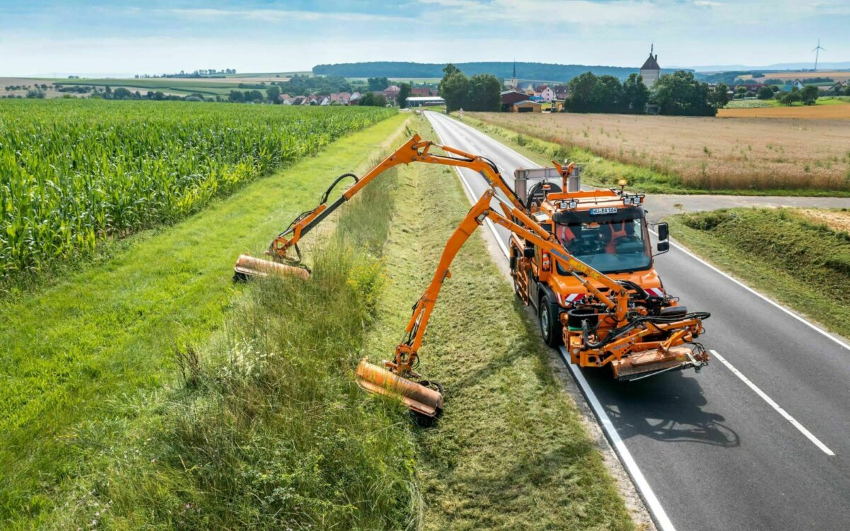 Ein Fahrzeug der Straßenmeisterei mäht den Grünstreifen neben einer Straße Ein Fahrzeug der Straßenmeisterei mäht den Grünstreifen neben einer Straße