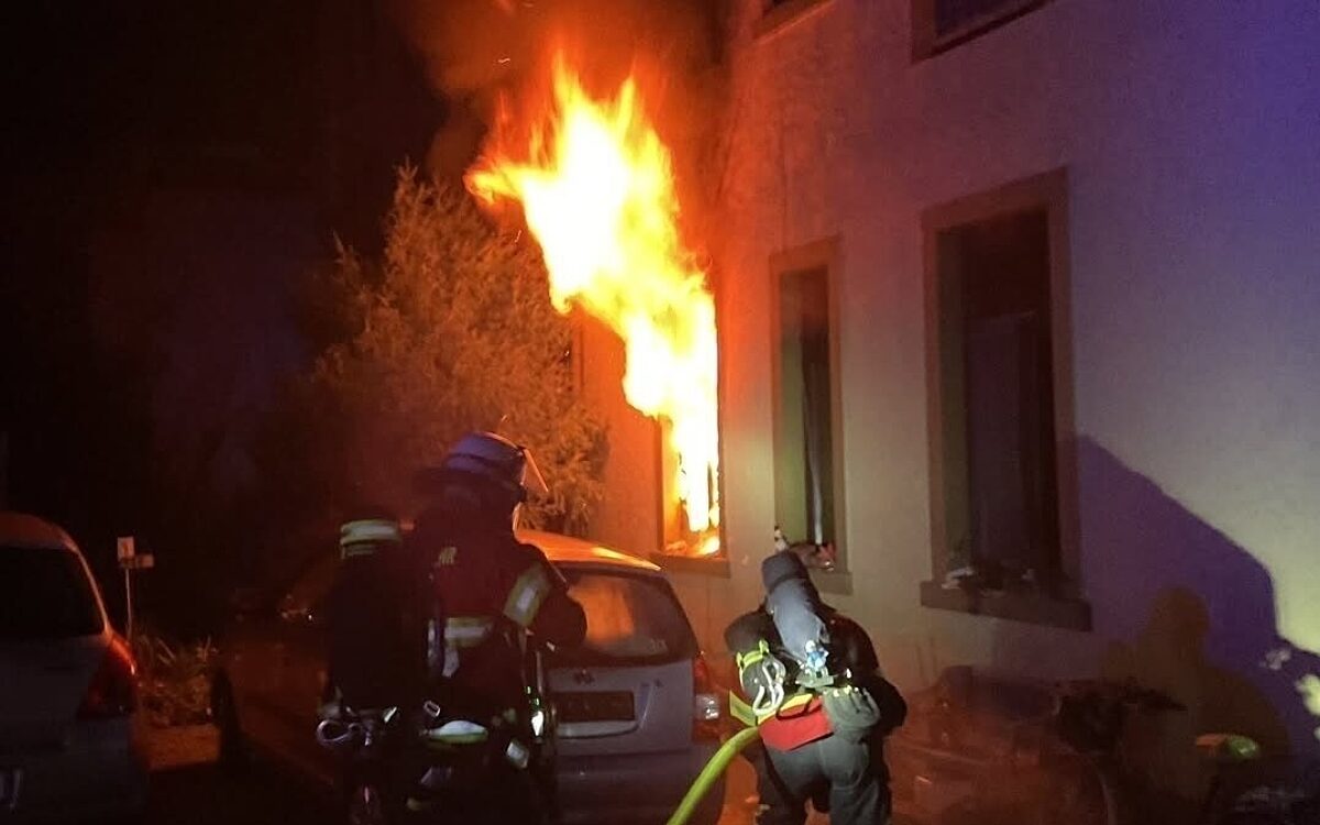 Feuerwehrleute kämpfen sich an die Flammen heran, die aus einem Fenster schlagen Feuerwehrleute kämpfen sich an die Flammen heran, die aus einem Fenster schlagen
