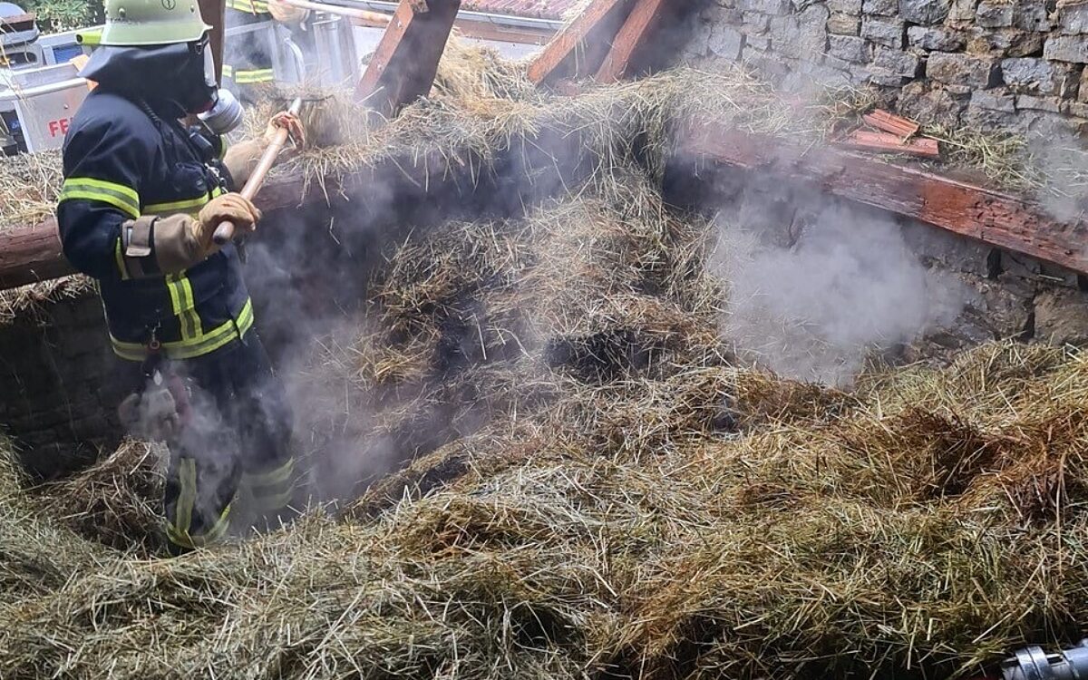 Ein Feuerwehrmann löscht qualmendes Heu in einer Scheune Ein Feuerwehrmann löscht qualmendes Heu in einer Scheune