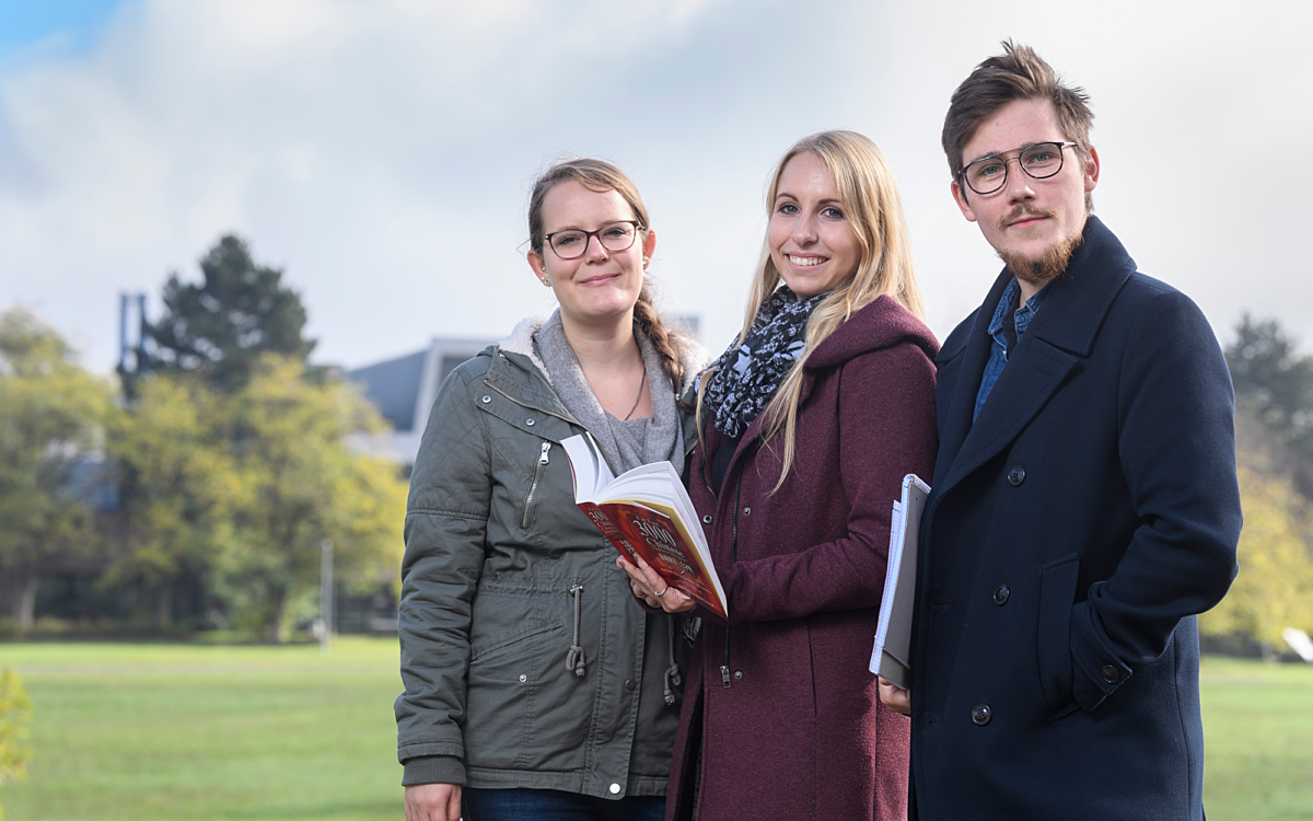 Drei Studenten mit einem Buch auf dem Campus der Uni Würzburg Drei Studenten mit einem Buch auf dem Campus der Uni Würzburg