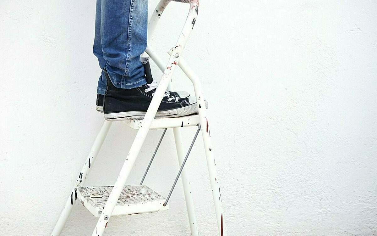 Ein mann mit schwarzen chucks steht auf einer weisen leiter Ein mann mit schwarzen chucks steht auf einer weisen leiter