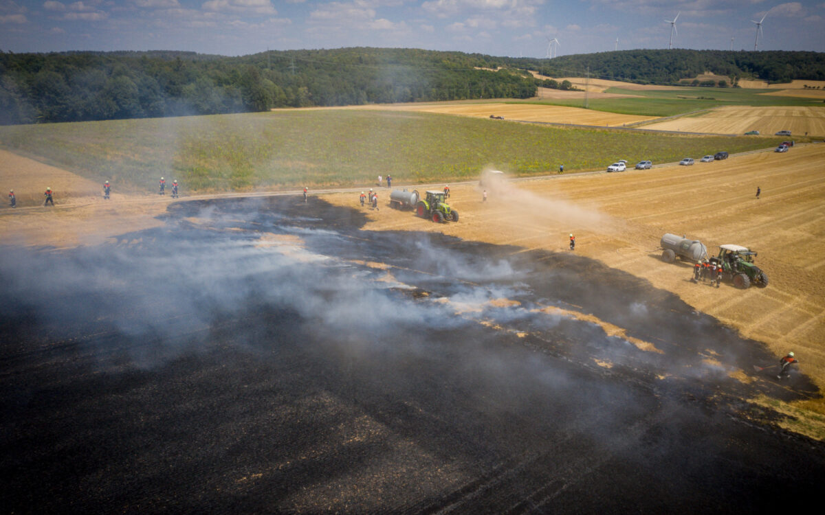 Ein Feld brennt. Mehrere Traktoren stehen zum Löschen bereit Ein Feld brennt. Mehrere Traktoren stehen zum Löschen bereit