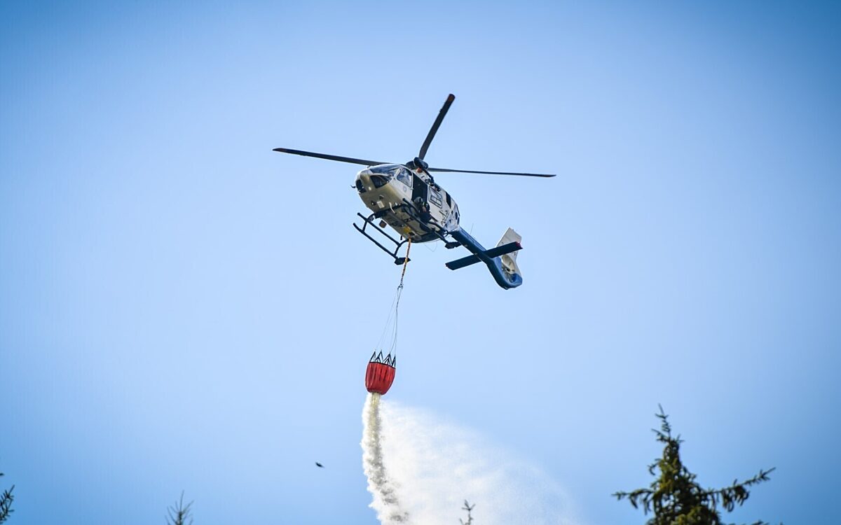 Ein Polizeihubschrauber mit Löschbehälter wirft Wasser über einem Waldbrand ab Ein Polizeihubschrauber mit Löschbehälter wirft Wasser über einem Waldbrand ab