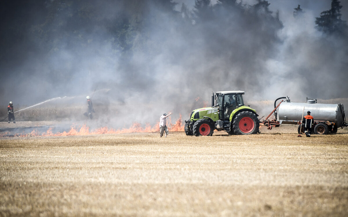 Ein Traktor steht auf einem brennenden Feld um beim Löschen zu helfen Ein Traktor steht auf einem brennenden Feld um beim Löschen zu helfen