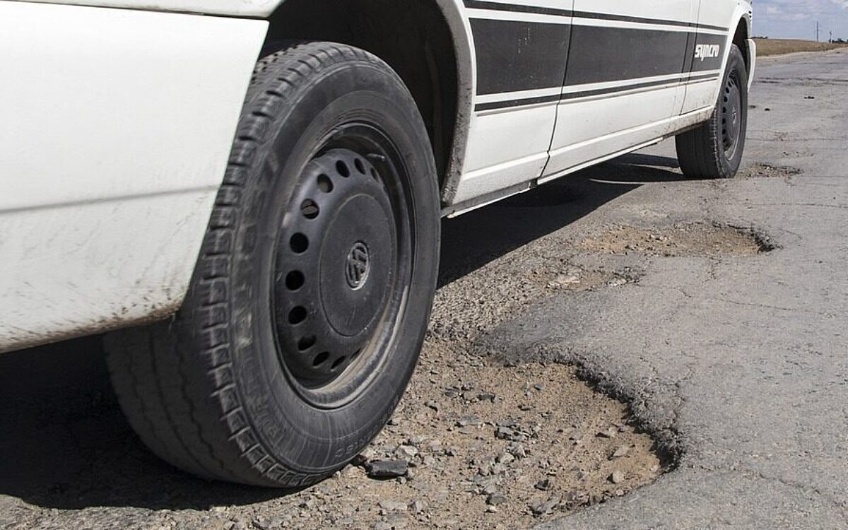 Ein Auto fährt über eine marode Straße mit vielen Schlaglöchern Ein Auto fährt über eine marode Straße mit vielen Schlaglöchern