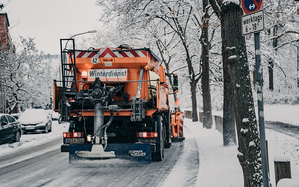 Ein orangefarbenes Winterdienst-Fahrzeug streut Salz auf verschneite Straße in Würzburg Ein orangefarbenes Winterdienst-Fahrzeug streut Salz auf verschneite Straße in Würzburg